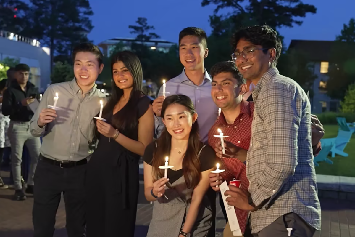 Group of six students holding lit candles on the Emory Quad